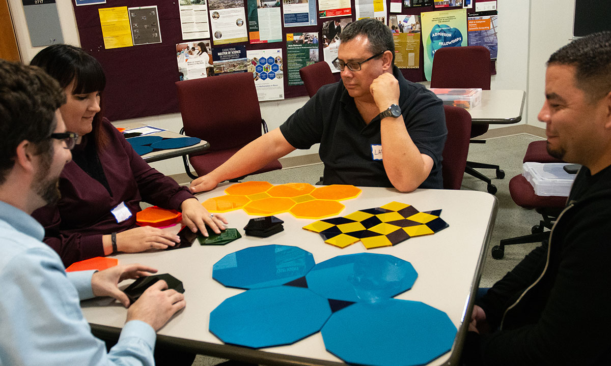 A group of 4 men and women sitting at a table working on a math puzzle